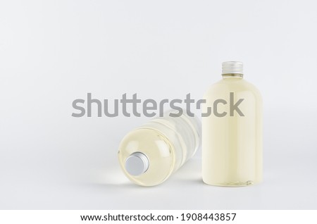 Set of two transparent plastic low thick bottles standing and lying with pale fresh drink or cosmetic essential oil and silver cap, mockup on white background,  front and side view.