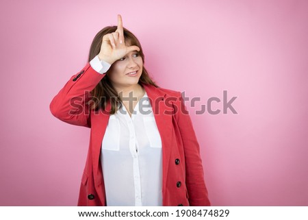 Young business woman over isolated pink background making fun of people with fingers on forehead doing loser gesture mocking and insulting.