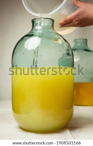 The process of making limoncello lemon liqueur at home. A man mixes lemon zest alcohol with sugar syrup in a ten-liter glass bottle.