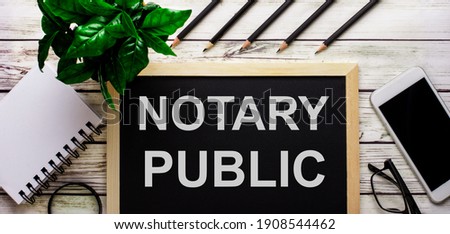 NOTARY PUBLIC is written in white on a black board next to a phone, notepad, glasses, pencils and a green plant. Royalty-Free Stock Photo #1908544462