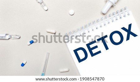 On a light background, a syringe, a stethoscope, vials of medicine, an ampoule and a white notepad with the text DETOX. Medical concept