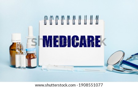 On a light background, a syringe, a stethoscope, vials of medicine, an ampoule and a white notepad with the text MEDICARE. Medical concept