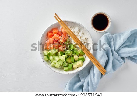 Salmon poke bowl with fresh fish, rice, cucumber, avocado with black and white sesame. White table. Food concept.