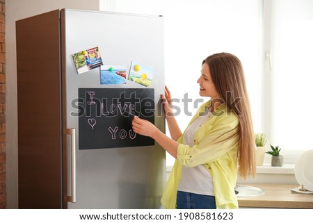 Young woman writing text I LOVE YOU on chalkboard in kitchen
