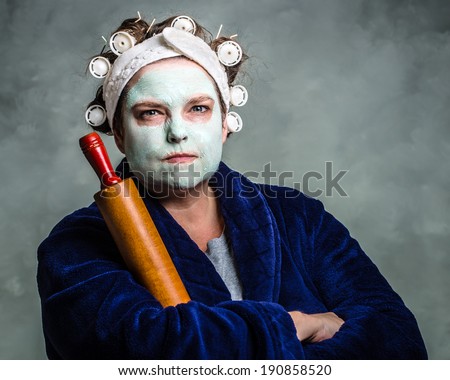 Mean and ugly housewife with facial mask, hair rollers and rolling pin Royalty-Free Stock Photo #190858520