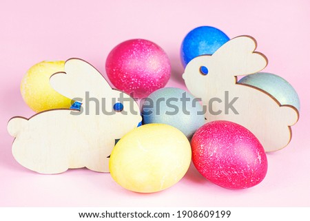 Funny wooden Easter Bunny with colorful eggs as symbols of a holiday on light pink background