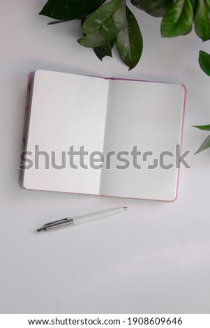 Top view of opened notebook with pen on light table with green plant in background