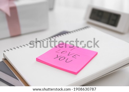 Memory sticker with phrase I Love You on notebook at table, closeup. Valentine's Day celebration