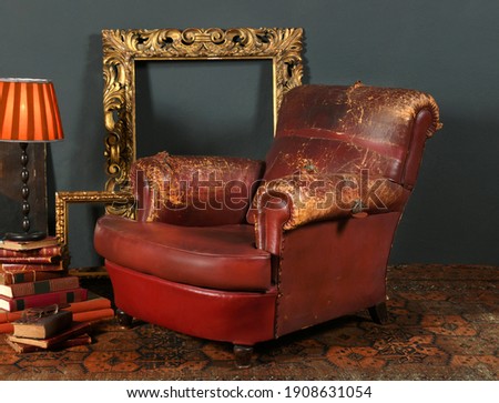 Old shabby red leather armchair placed near vintage decorative frames and lamp in room with retro style interior Royalty-Free Stock Photo #1908631054