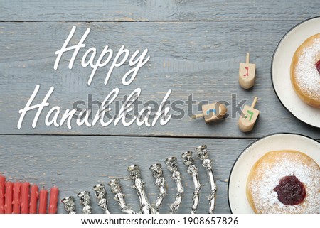 Happy Hanukkah. Flat lay composition with menorah, red candles, dreidels and sufganiyot on grey wooden table