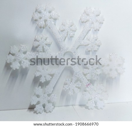 a white snowflake with silver sequins and a shadow of light on a white background