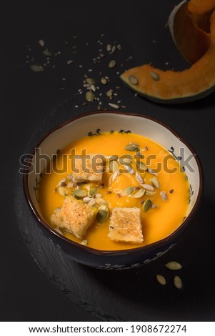 Pumpkin cream soup with seeds and croutons on a black background