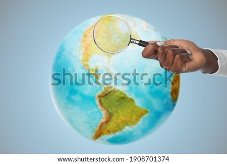 investigation, discovery and search concept - hand with magnifying glass over earth planet on blue background Royalty-Free Stock Photo #1908701374