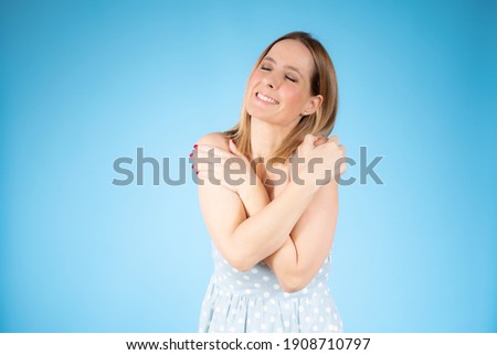 Portrait of a pretty young woman in blue dress hugging herself. Concept of selfish emotion.