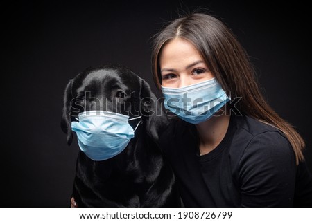 Portrait of a Labrador Retriever dog in a protective medical mask with a female owner. The picture was taken in a photo Studio