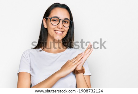 Young hispanic woman wearing casual white t shirt clapping and applauding happy and joyful, smiling proud hands together 