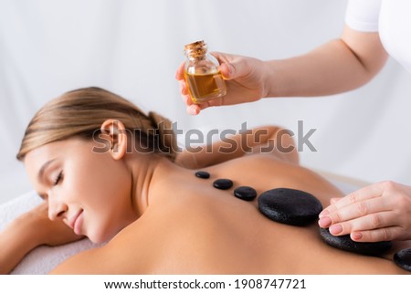 masseur holding bottle with oil near client getting hot stone massage Royalty-Free Stock Photo #1908747721