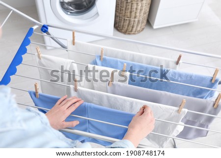 Woman hanging clean laundry on drying rack indoors, closeup