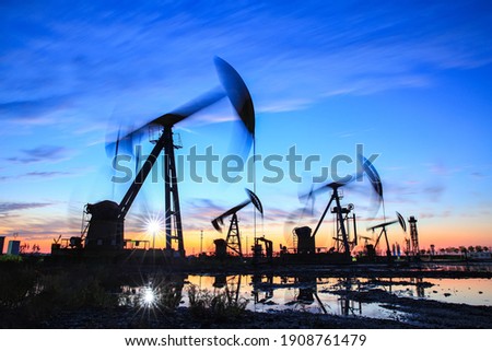 Oil field site, in the evening, oil pumps are running, The oil pump and the beautiful sunset reflected in the water, the silhouette of the beam pumping unit in the evening. Royalty-Free Stock Photo #1908761479
