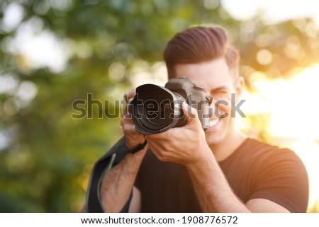 Photographer taking picture with professional camera in countryside, focus on lens