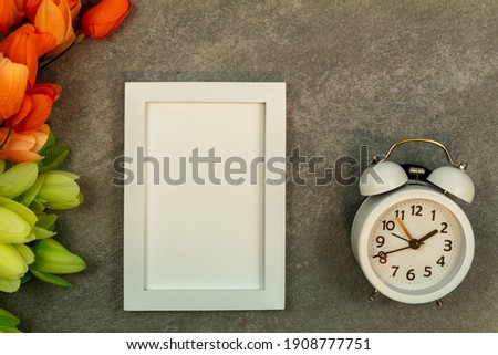 White frame mockup and alarm clock on gray granite with tulips flat lay for Spring, Daylight Saving Time