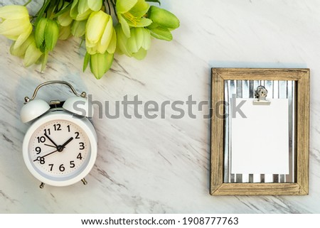 White blank note mockup on marble alarm clock tulips flat lay for Spring, Daylight Saving Time