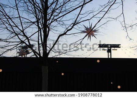 Silhouette of trees and a star-shaped lantern against the sunset behind the fence with light reflecting circles