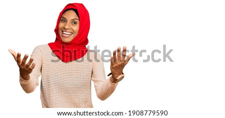 Young african american woman wearing traditional islamic hijab scarf smiling cheerful offering hands giving assistance and acceptance. 