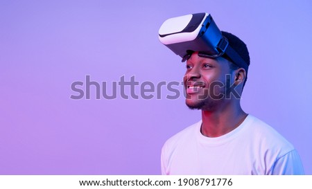 Smiling African American Guy Wearing VR Glasses Looking Aside Over Purple Background, Enjoying Modern Technologies For Entertainment, Excited Man Experiencing Virtual Reality, Neon Light, Panorama