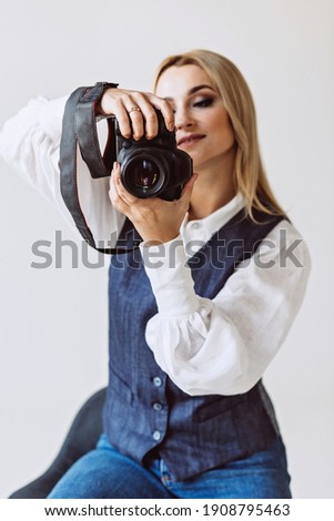A beautiful woman photographer in a denim casual outfit and a white blouse with voluminous sleeves with a camera in her hands. Hobbies. Soft selective focus.