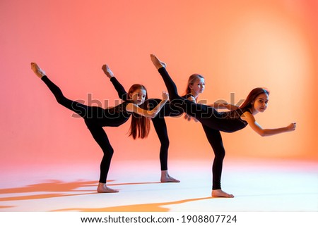 group of three ballet girls in black tight-fitting suits dancing on a red background with their long hair down.