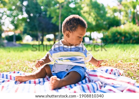 Adorable african american toddler sitting on the grass at the park.