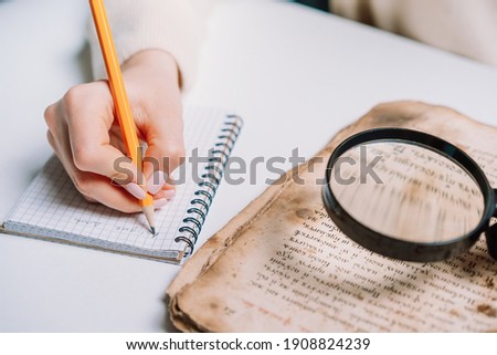 Researcher examines antique book with magnifying glass. Scientific translation of ancient literature. Studying manuscript with ancient writings. High quality 