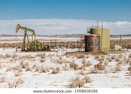 Lonely oil pump in the middle of a snow covered desert landscape on clear day in rural New Mexico