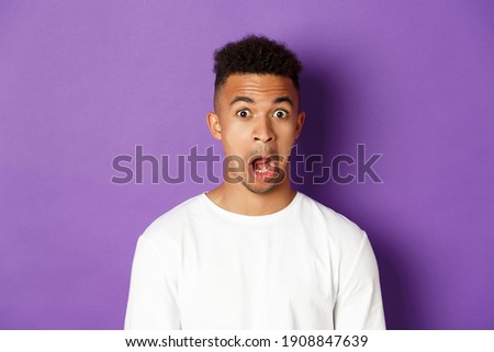 Close-up of impressed african-american man, drop jaw and stare at something amazed, standing over purple background