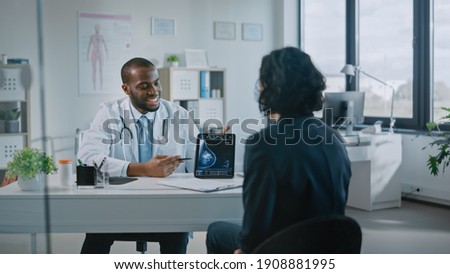 African American Medical Doctor Showing Mammography Test Results to a Patient on a Tablet Computer in a Health Clinic. Friendly Assistant Explains Importance of Breast Cancer Prevention Screening. Royalty-Free Stock Photo #1908881995