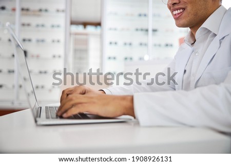 Cropped photo of a smiling male optician in a lab coat working on his computer Royalty-Free Stock Photo #1908926131