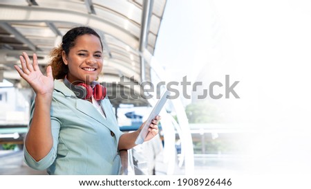 Portrait of young business woman way to work on city street with tablet and headphones for say hi her friends. Walking outdoors and working outdoors. Dreams and successful concept