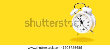 White bell alarm clock hovering over yellow background. 5 to 12 clock concept isolated Royalty-Free Stock Photo #1908926485