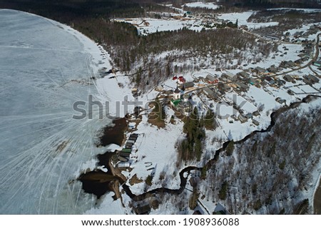 Aerial view of the lake and the snowy coast in winter against the blue sky. Photo of the northern nature from the drone.