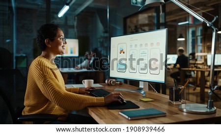 Young Latina Designer Working on a Desktop Computer in Creative Office. Beautiful Diverse Multiethnic Female is Developing a New App Design and User Interface in a Digital Graphics Editing Software. Royalty-Free Stock Photo #1908939466