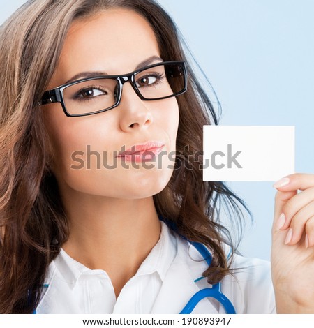 Portrait of happy smiling young female doctor showing blank business card or invitation, over blue background