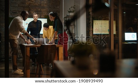 Diverse Multiethnic Team are Having a Conversation in a Meeting Room Behind Glass Walls in a Creative Office. Colleagues Lean On a Conference Table and Discuss Business, App User Interface and Design. Royalty-Free Stock Photo #1908939490
