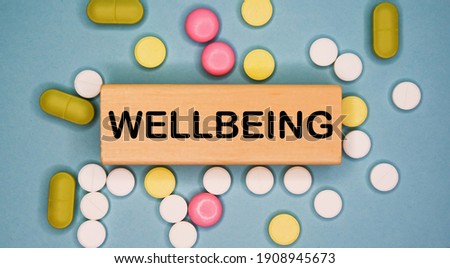 WELLBEING written on wooden block on a blue background among multicolored pills. Medical concept