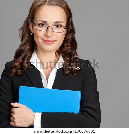Portrait of happy smiling young business woman with blue folder, over gray background