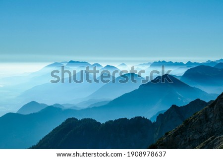 A close up view on the Alpine chains shrouded in the morning fog, seen from the top of Mittagskogel in Austria. Clear and sunny day. Sharp peaks around. Sun is shining above the high peaks. Serenity Royalty-Free Stock Photo #1908978637