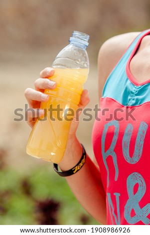 Detail photo of a sporty woman holding a bottle of orange juice during her training - healthy lifestyle