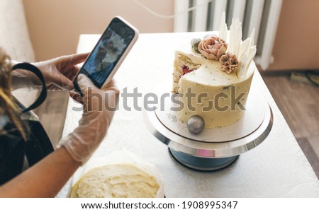 a young pastry chef girl in a gray apron takes pictures of a prepared cake.