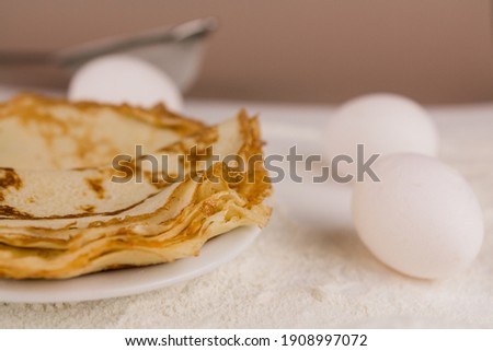 a beautiful round thin pancakes on the kitchen table with flour and whisk and eggs
