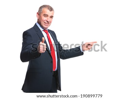 mid aged business man pointing to his side and showing the thumb up gesture while smiling for the camera . isolated on a white background